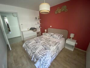 Une chambre à coucher comprenant un lit, des tables de chevet, une commode, un miroir et un mur d’accent de couleur rouge.