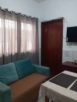 Una habitación con sofá, una mesa, una puerta de madera y televisor instalado en la pared.