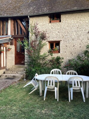 Ein Steinhaus mit einer Holztür und Fenstern, ein kleiner Garten mit Tisch und Stühlen sowie eine Rasenfläche.
