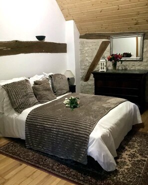 A bedroom with a bed, a dresser, a mirror, and a small table with flowers. - New Listing (Léry)