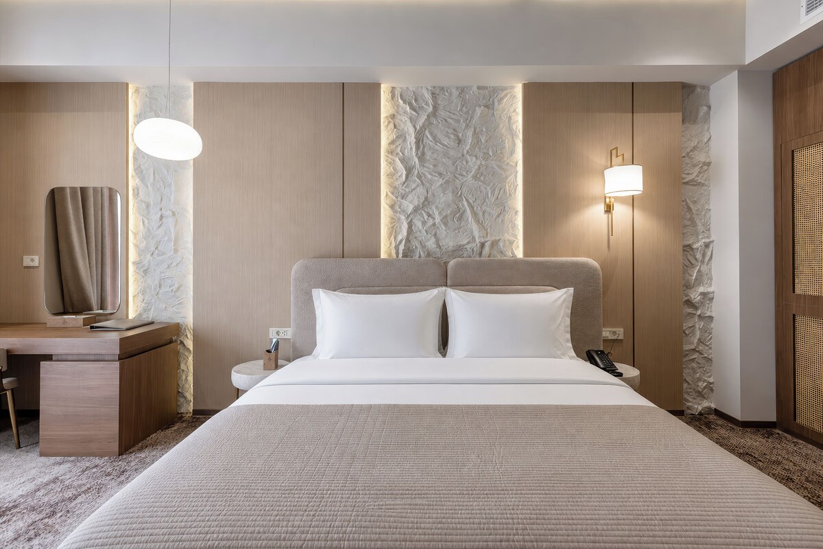 A hotel room with a bed, bedside tables, a desk, and a mirror.