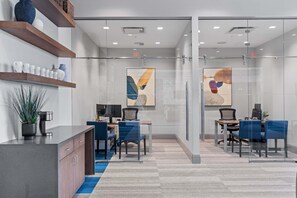 Un espacio de oficina moderno con divisiones de vidrio, estanterías de madera y alfombra azul.
