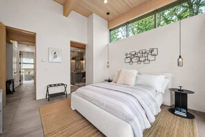 A modern bedroom with a large bed, a bedside table, a wall-mounted light fixture, and a view of the outdoors through a window. - Modern Mountain Escape - 2 Acres - Bike/Ski (Fraser)