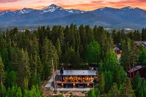 A modern lodge with a large deck, surrounded by dense forest and mountains in the background. - Modern Mountain Escape - 2 Acres - Bike/Ski (Fraser)