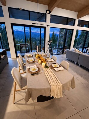 A modern dining area with a long table set for a meal, large windows offering a view of the outdoors, and a cozy seating area with a sofa. - Modern Mountain Escape - 2 Acres - Bike/Ski (Fraser)