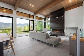 Een modern interieur met een open haard, een bank en een eethoek met uitzicht op de bergen.