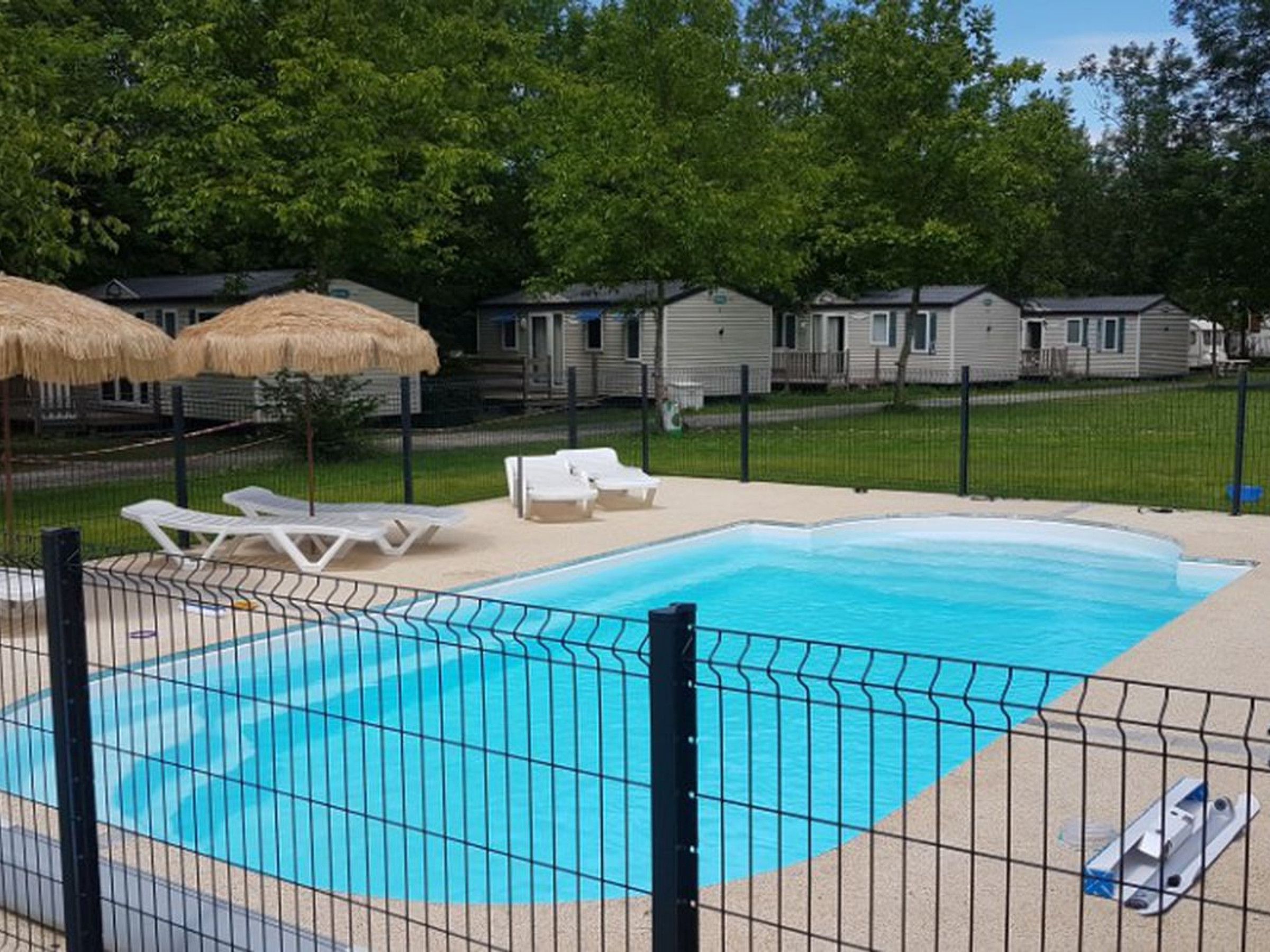 A swimming pool with a fenced area, lounge chairs, and thatched umbrellas.