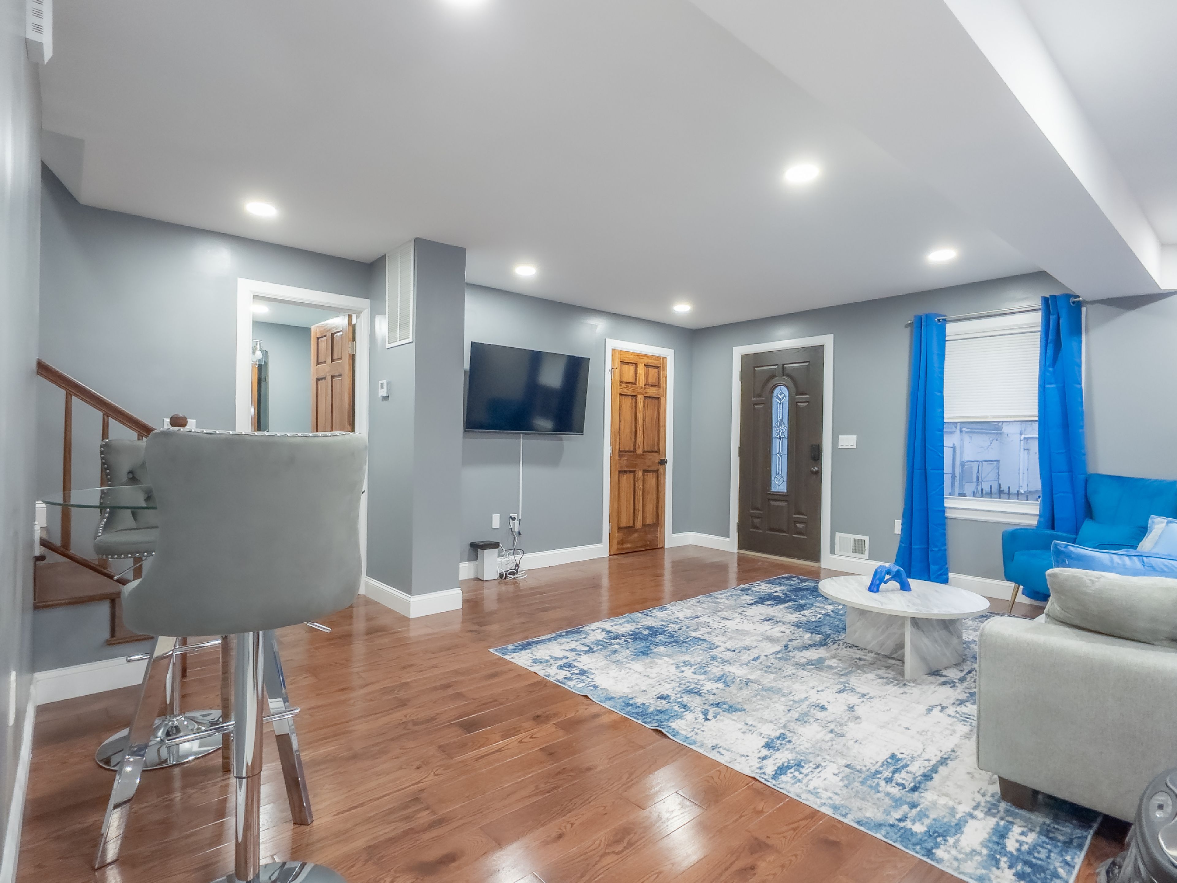 A modern living room with hardwood flooring, a grey sofa, a coffee table, and a flat-screen TV mounted on the wall.