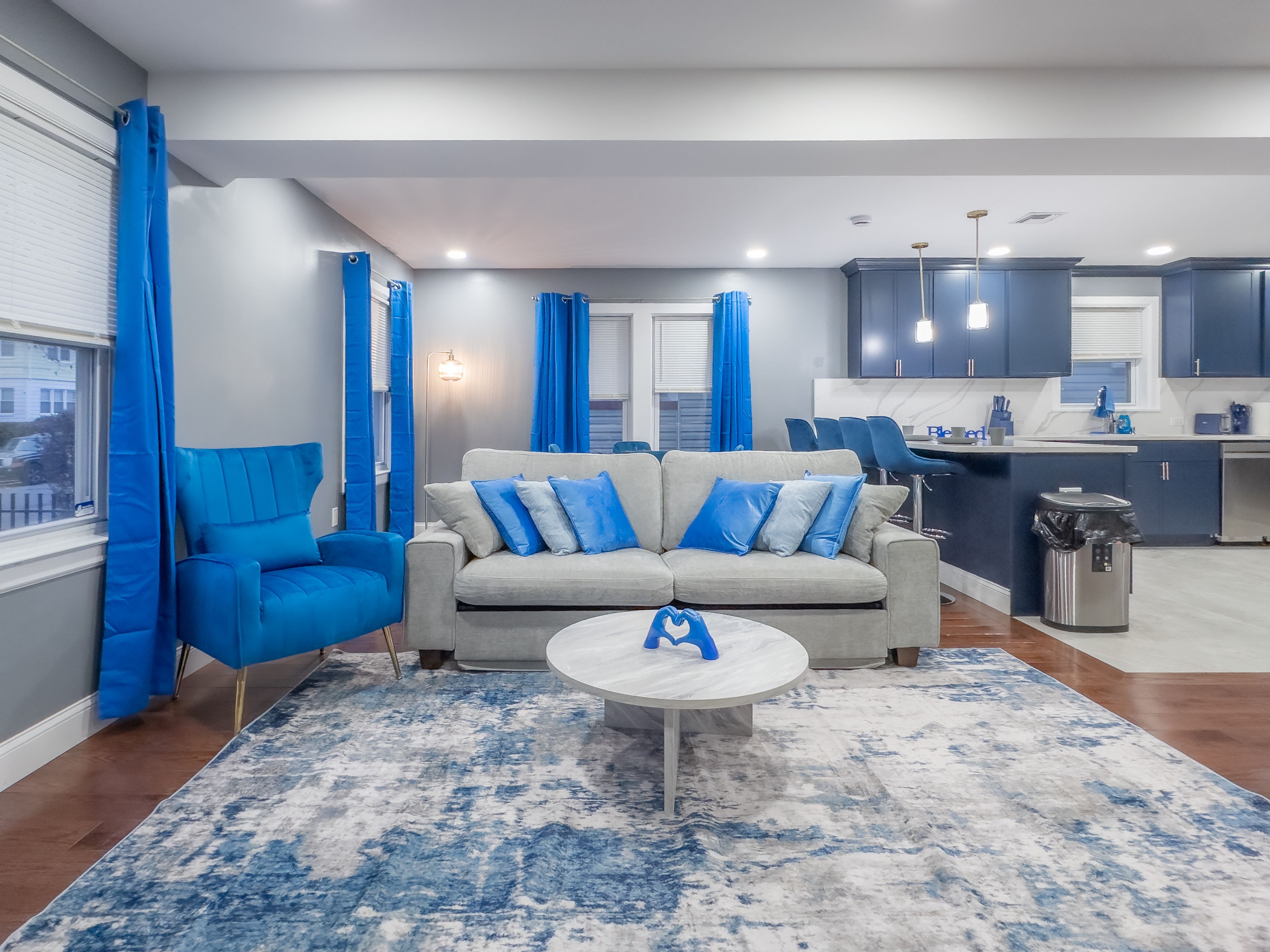 A modern living room with a grey sofa, blue cushions, a coffee table, and a patterned rug.