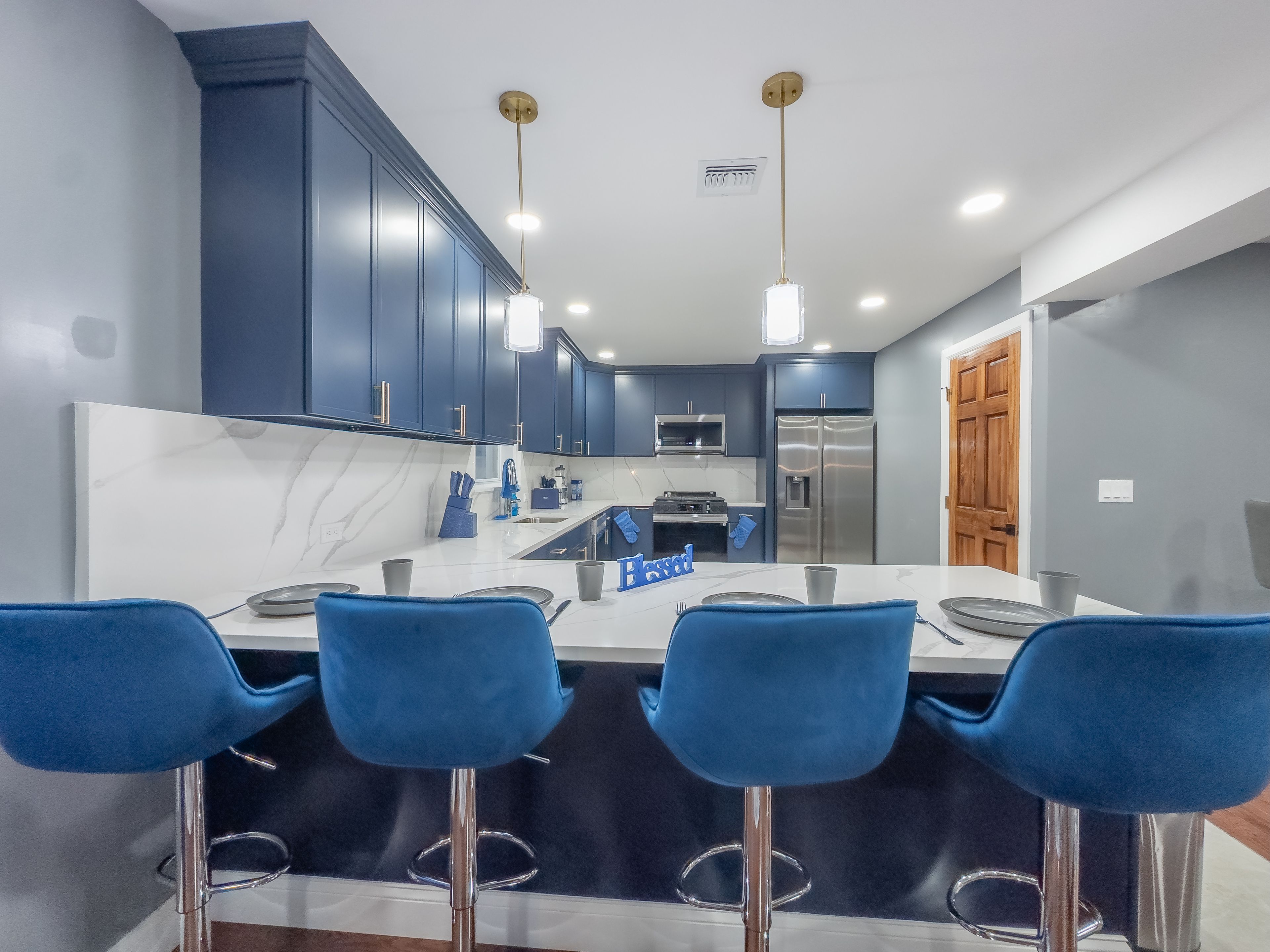 A modern kitchen with dark blue cabinets, a central island with bar stools, stainless steel appliances, and pendant lighting.