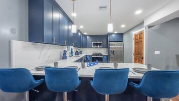 A modern kitchen with dark blue cabinets, a central island with bar stools, stainless steel appliances, and pendant lighting.
