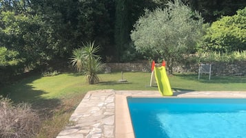 Una piscina con bordo in pietra, uno scivolo e un muro di pietra sullo sfondo.