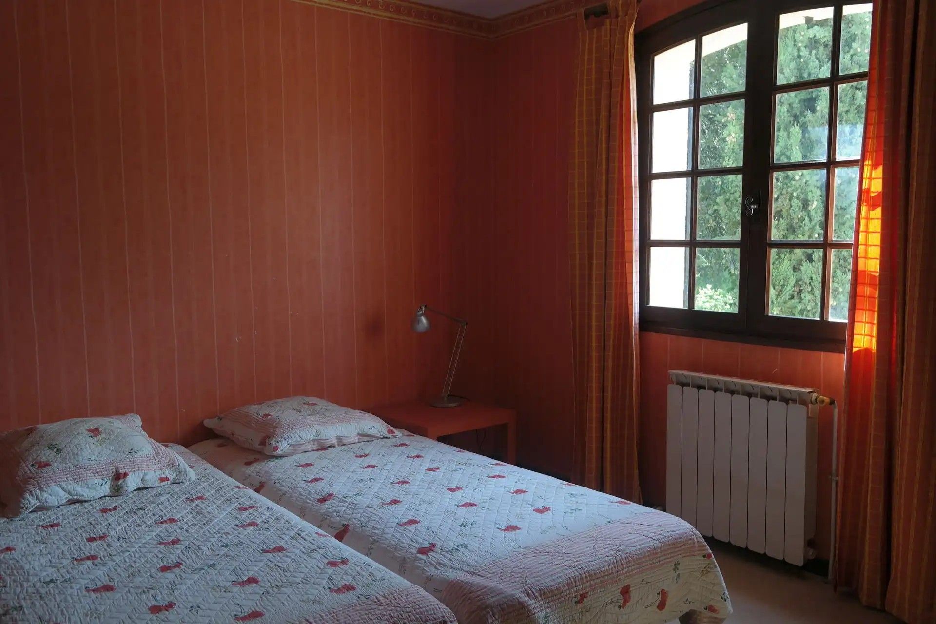 Une chambre avec deux lits, un radiateur, une fenêtre avec des rideaux et une lampe.