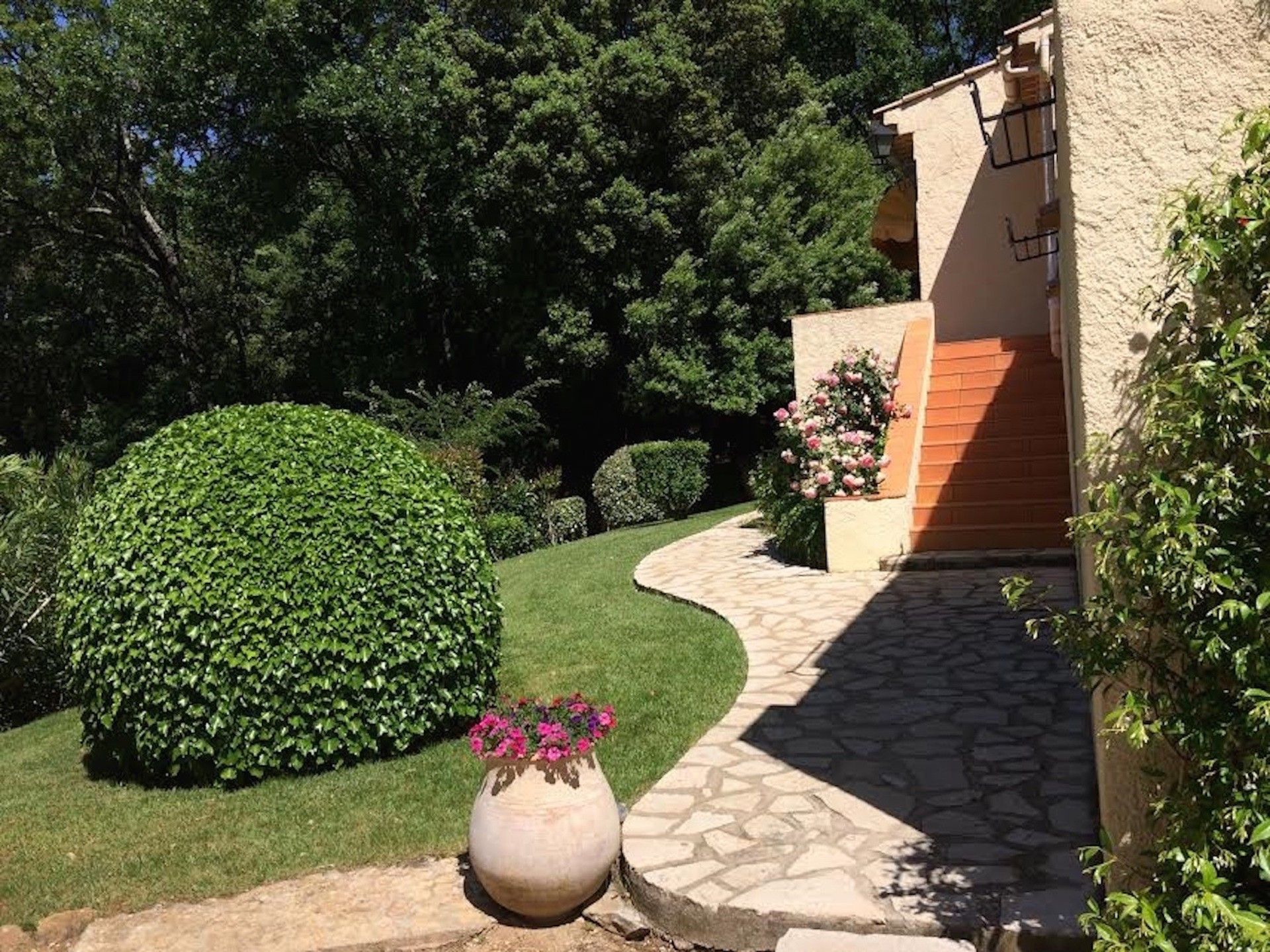 Un jardin aménagé avec un sentier en pierre menant à un bâtiment dont la façade est recouverte d’enduit.