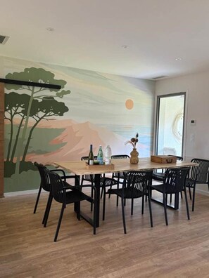A dining area with a mural, a wooden table, black chairs, and a window. - Vrbo Property (Andernos-les-Bains)