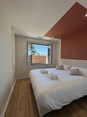 A bedroom with a large bed, a window, and a sloped ceiling. - Vrbo Property (Andernos-les-Bains)