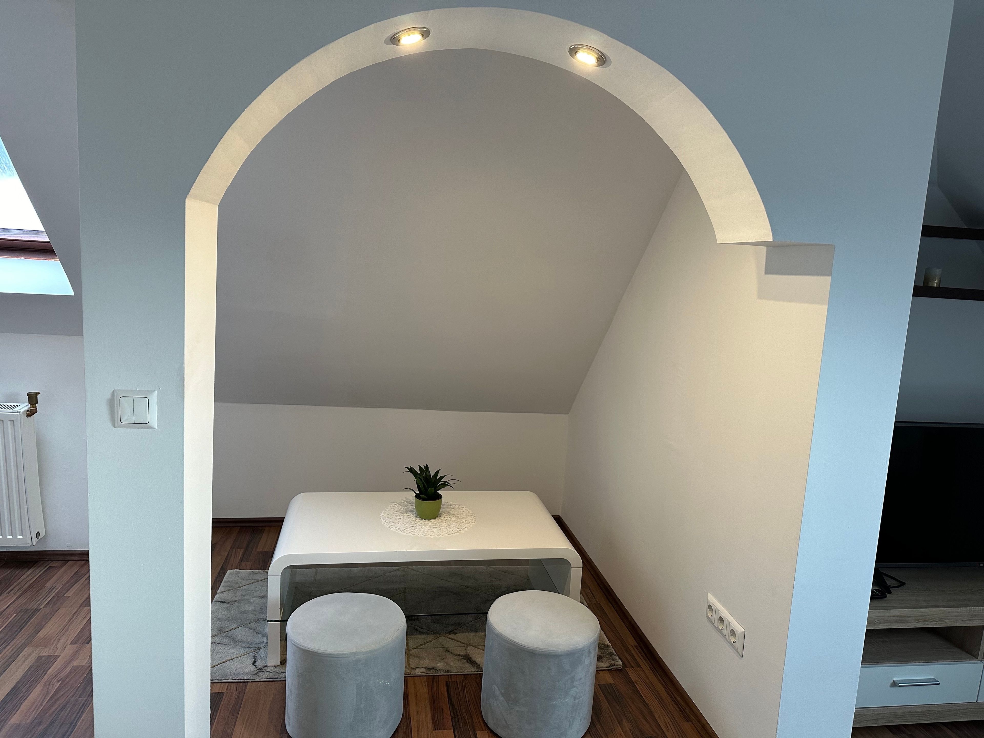 A modern interior with a white arched ceiling, a small table with a green plant, and two grey ottomans.