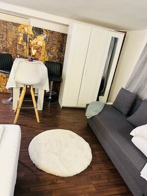 Una sala moderna con un tapete redondo blanco, un sofá gris, una mesa de comedor con una silla negra y un armario con espejo.