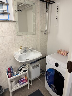 Ein Badezimmer mit einem weißen Waschbecken, einem Spiegel, einer Dusche und einer Waschmaschine.