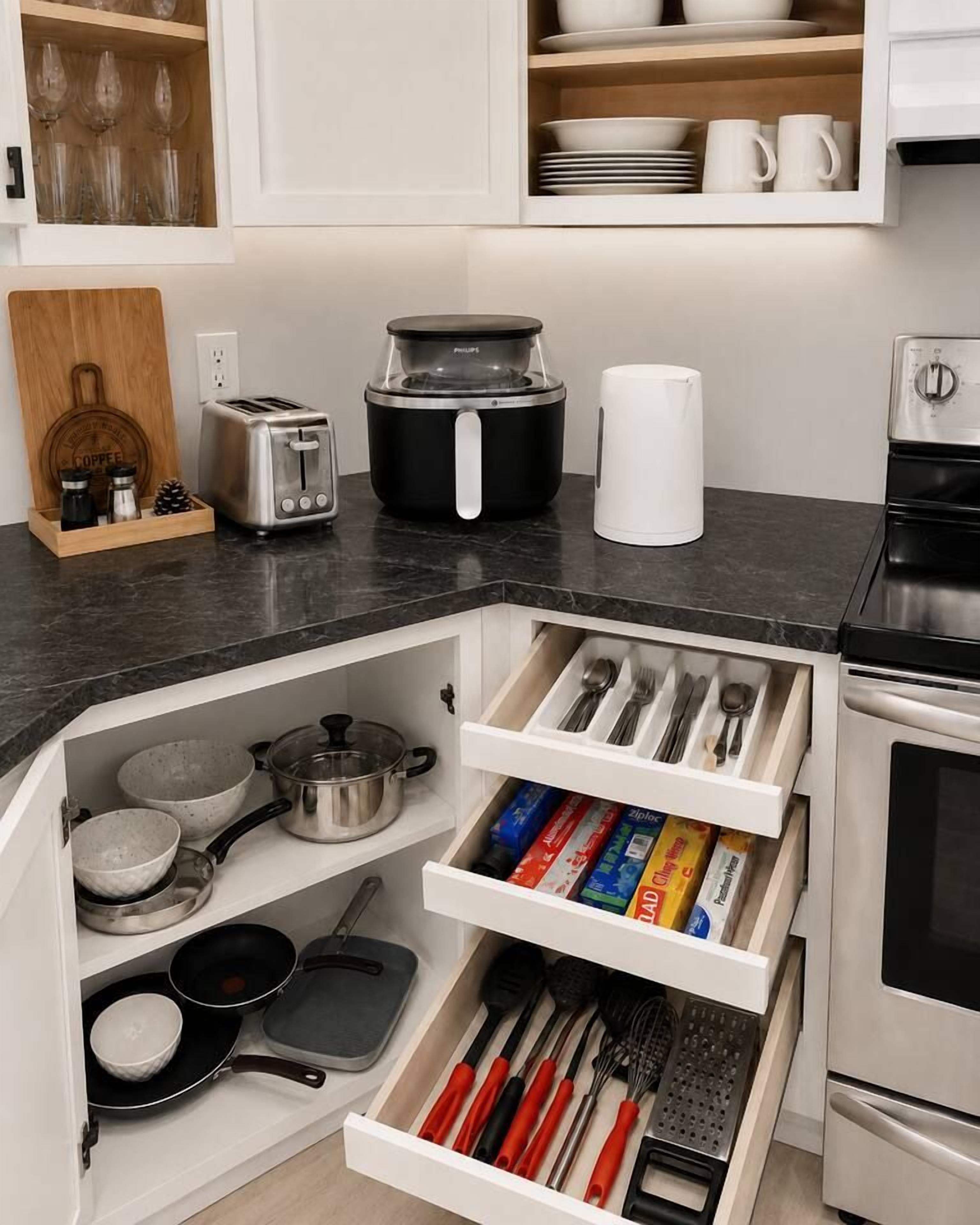 Een keuken met een zwart aanrecht, witte kastjes en een ingebouwde lade-organizer.