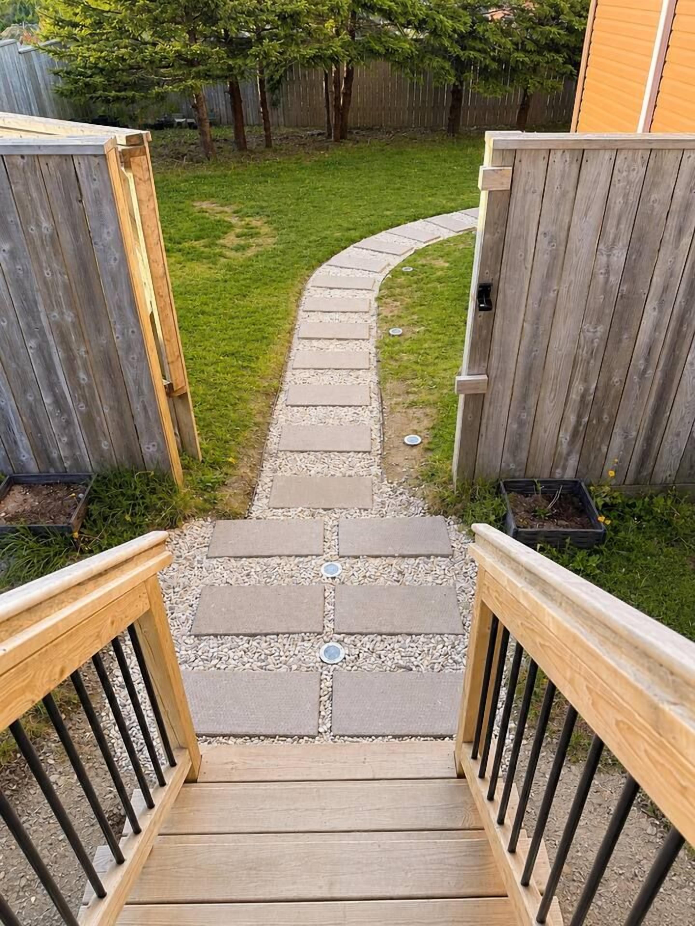 Un escalier en bois mène à un jardin à l’arrière de la maison, où se trouve un chemin pavé de pierres.