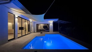 Ein modernes Haus mit Swimmingpool, Glasüren und einer überdachten Terrasse.