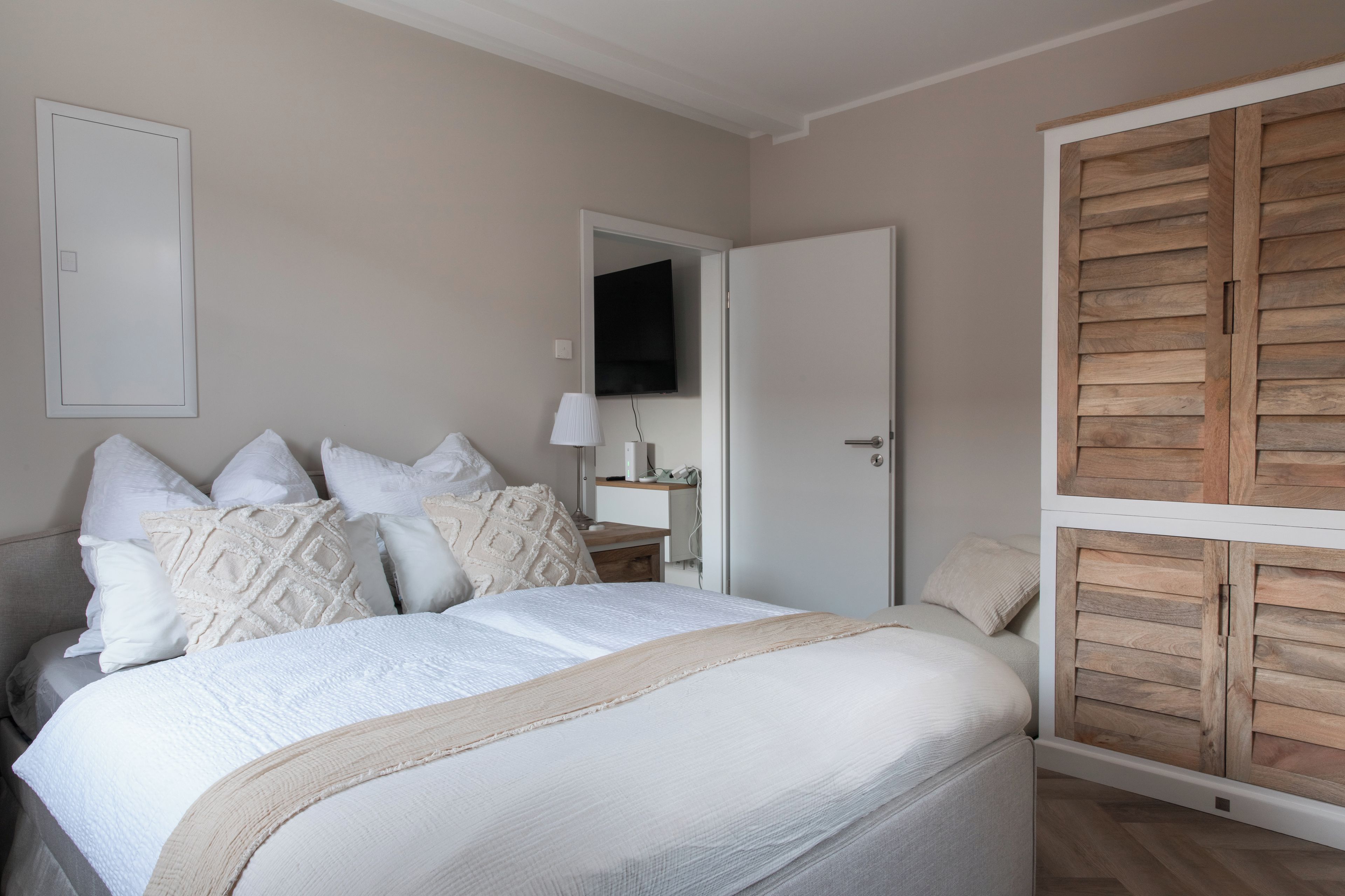 Un dormitorio con cama, almohadas, mesita de noche, lámpara y armario de madera.