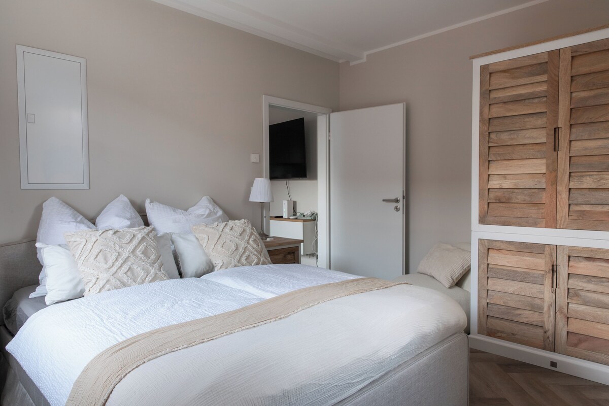 Une chambre à coucher avec un lit, des oreillers, une table de chevet, une lampe et une armoire en bois.