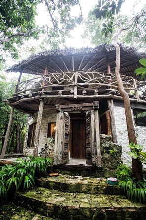 Ein traditionelles Holzhaus mit einem Strohdach, umgeben von üppigem Grün.