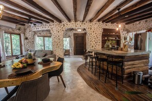 Ein rustikaler Innenraum mit einer Steinwand, Holzbalken, einem Essbereich mit Tisch für zwei Personen und einer Bar mit Hockern.