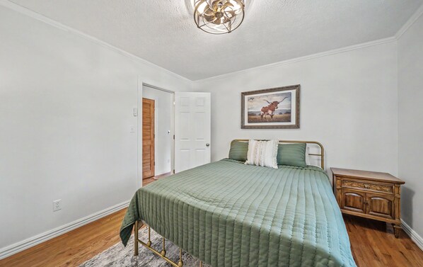 A bedroom with a bed, a wooden nightstand, a framed picture on the wall, and a door. - Little Southern House at Southern Silos, Farmhouse getaway near Rolla, Missouri (Rolla)