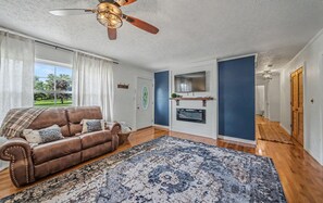 A living room with a brown leather sofa, a blue patterned rug, a ceiling fan, and a TV mounted on a blue wall. - Little Southern House at Southern Silos, Farmhouse getaway near Rolla, Missouri (Rolla)