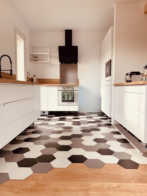 A narrow kitchen with white cabinets, a black range hood, and a hexagonal patterned floor. - New Listing (Le Verdon-sur-Mer)