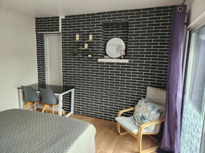 Ein Zimmer mit Ziegelwand, Schreibtisch mit Stühlen, einem Bett und einem Fenster mit Vorhängen.