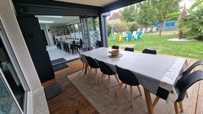 Ein offener Wohnbereich mit Esstisch und Stühlen, eine durch Glastüren sichtbare Küche und ein Blick auf einen Garten mit Gartenmöbeln.