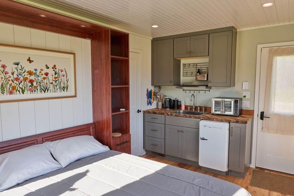 Une chambre avec un lit, une petite kitchenette équipée d’un réfrigérateur, et une porte donnant sur une autre pièce.