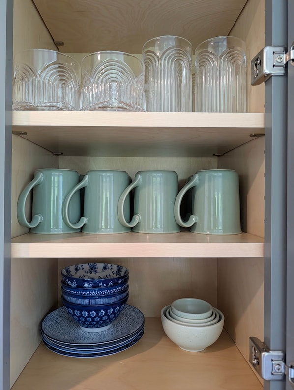 Une étagère avec des verres en verre transparent, des tasses en céramique verte et des bols à motifs bleus.