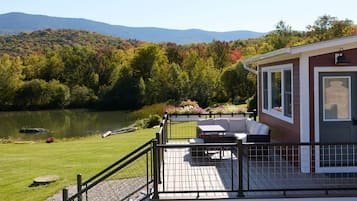 A deck with outdoor furniture overlooking a lake and forested hills.