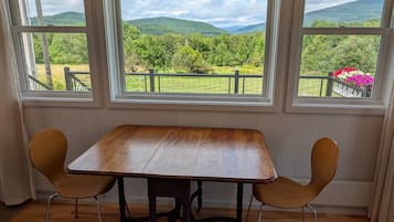 A room with a wooden table and two chairs, large windows with a view of green hills.