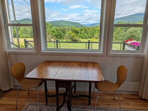 Une pièce avec une table en bois et deux chaises, de grandes fenêtres donnant sur des collines verdoyantes.