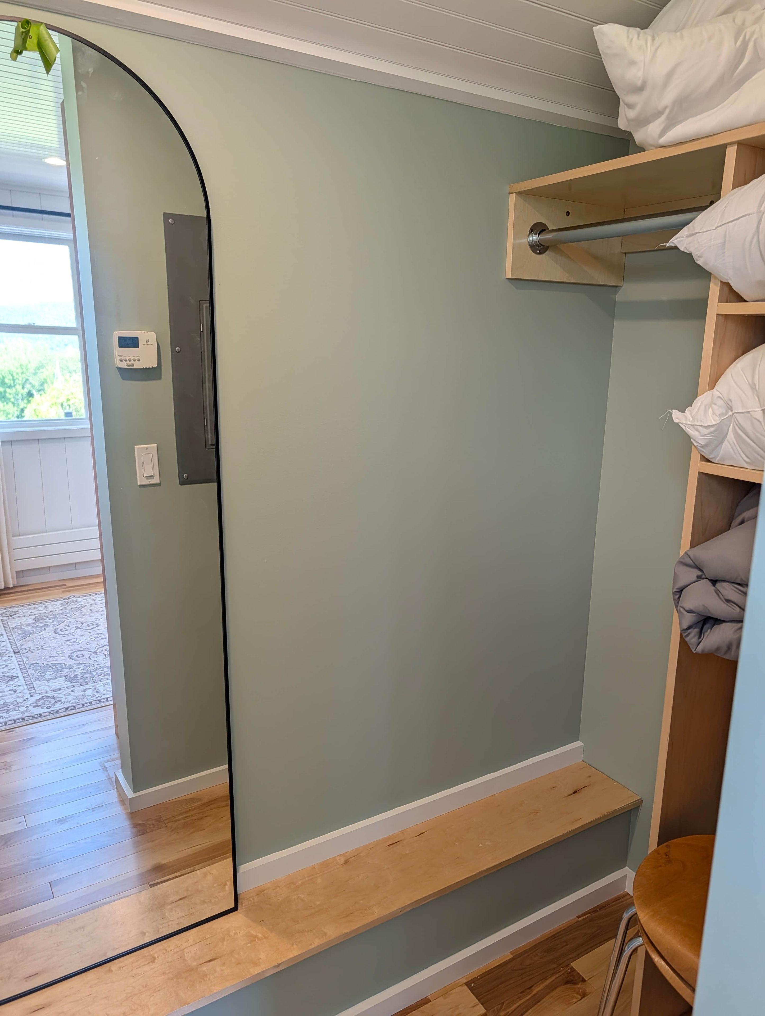 A room with a wooden floor, a built-in bench, a wall-mounted heater, and a window with blinds.