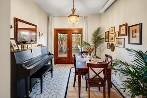Une pièce comprenant un piano, une table à manger, des chaises, un lustre et des tableaux encadrés accrochés au mur.