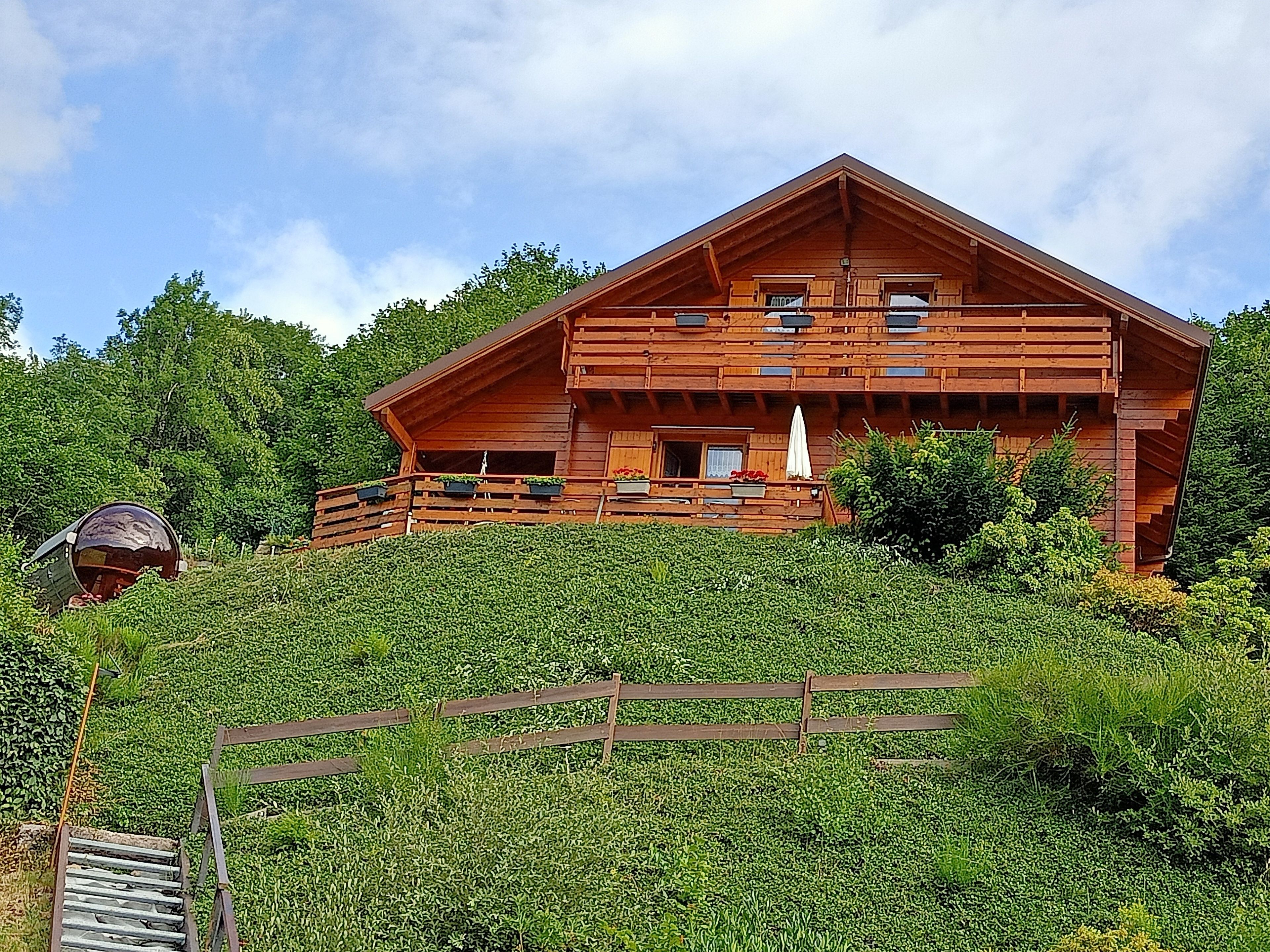 A wooden cabin with a balcony, surrounded by lush greenery.
