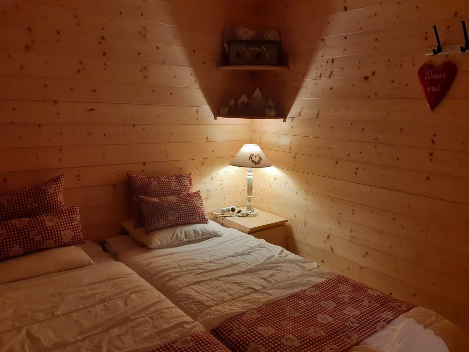 Une chambre confortable avec deux lits, une lampe de chevet et une décoration en forme de cœur accrochée au mur.