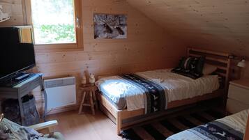 A cozy room with a bed, a desk with a television, a radiator, and a window with a view of greenery.