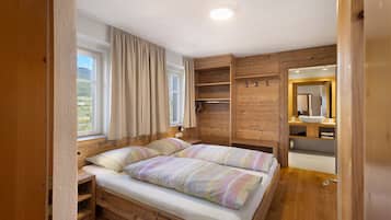 Une chambre avec un lit en bois, une fenêtre avec des rideaux, une étagère intégrée et une salle de bain avec un miroir et un lavabo.