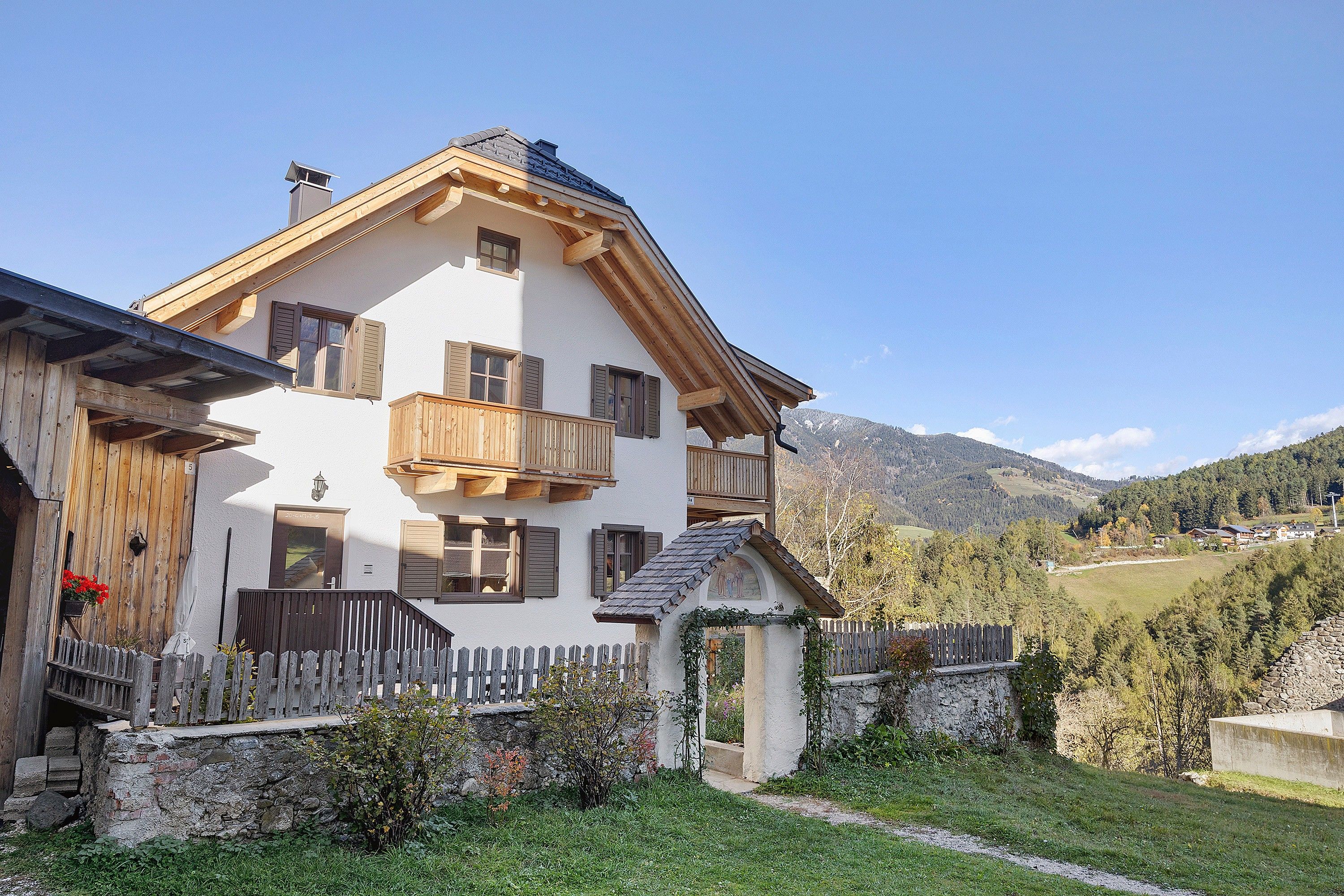 Un chalet à deux étages doté d’un balcon, d’un mur en pierre et d’une clôture en bois.