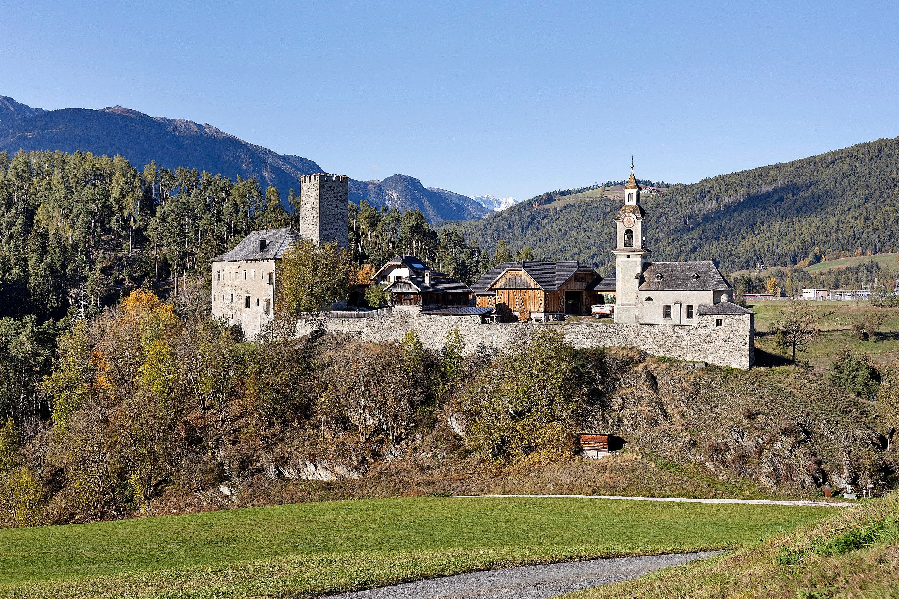 Un château de pierre historique, doté de nombreuses tours et d’une église, entouré d’un paysage boisé et de montagnes.