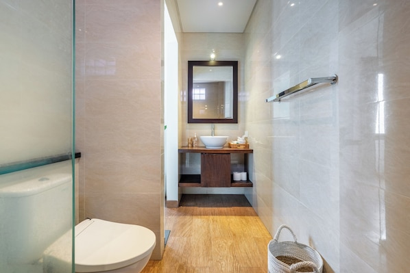 A modern bathroom with a glass shower enclosure, a white toilet, a wooden vanity with a mirror, and a towel rack. - Chic 2BR Private Pool Villa Seminyak, Enclosed AC Living & Fast Wi-Fi (Badung)