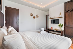 A hotel room with a bed, a TV, a small table with a plant, and decorative wall art. - Chic 2BR Private Pool Villa Seminyak, Enclosed AC Living & Fast Wi-Fi (Badung)
